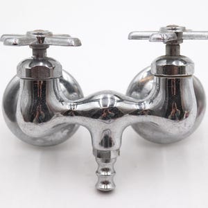 May include: A vintage chrome faucet with two cross-shaped handles. The faucet has a curved spout and a central outlet. The shiny metal reflects the surrounding environment. This plumbing fixture is designed for a sink or basin.