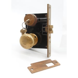 May include: A vintage brass door knob and lock set with two keys. The lock is black and the knob is round with a flat front. The set includes a separate strike plate.