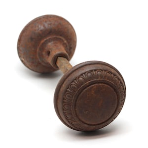 Può includere: Una vecchia maniglia per porta in metallo marrone rugginoso con un anello decorativo attorno al bordo.