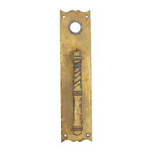 May include: Antique brass door pull with a rectangular backplate. The pull features a detailed, twisted handle design. The backplate has a circular hole and decorative edges. The brass has a weathered appearance, suggesting age and use.
