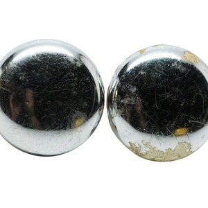 May include: Two round, silver-colored metal knobs. One knob is shiny and the other has some wear and tear.