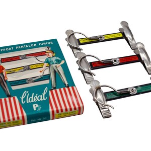 May include: A vintage box of Ideal trouser hangers, featuring a red, white, and blue striped design. The box has a blue background with an illustration of two children using the hangers. The text on the box reads "Le Support Pantalon Junior L'ideal P.t. Ref. No. 30".