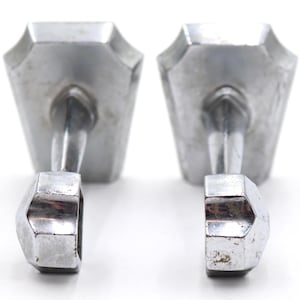 May include: A pair of silver-toned metal cufflinks featuring a trapezoidal face with a smooth, reflective surface. Each cufflink has a straight post connected to a smaller, faceted, hexagonal-shaped toggle mechanism at the base for fastening.