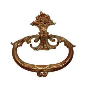 Pode incluir: Puxador de gaveta ornamental em tom bronze com um design floral decorativo. O puxador apresenta uma pega curva e uma peça superior elaborada com folhas e volutas detalhadas. Uma peça de hardware de estilo vintage para restauração de móveis.