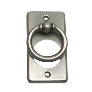 Puede incluir: Una placa rectangular plateada con un asa redonda en forma de anillo. El asa tiene una pequeña bola en la parte superior.