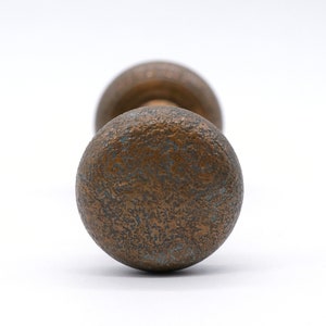 Op de afbeelding: Close-up van een vintage bronzen deurknop met een getextureerd oppervlak. De knop heeft een ronde vorm en een aangetaste, verouderde uitstraling, met hints van blauwgroene patina. De achtergrond is effen wit.