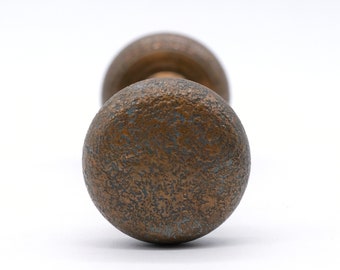 May include: Close-up of a vintage bronze door knob with a textured surface. The knob has a round shape and a tarnished, aged appearance, with hints of blue-green patina. The background is plain white.
