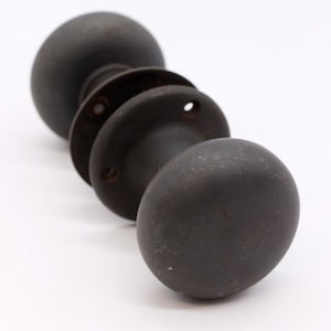 May include: A black metal door knob with two round knobs. The knobs are smooth and have a slightly worn finish.