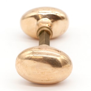 May include: A pair of oval-shaped door knobs with a polished brass finish. The knobs are connected by a metal rod.