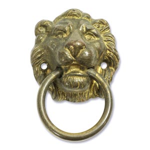 May include: A vintage brass lion head door knocker with a ring handle. The lion's face is detailed with a textured mane and open mouth. Two screw holes are visible on either side of the head.