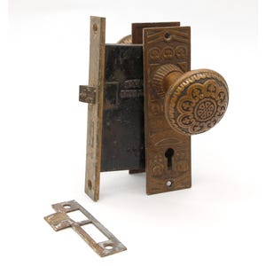 Puede incluir: Conjunto de pomo y cerradura de puerta de latón antiguo con un diseño floral decorativo. El pomo tiene una cerradura y la cerradura tiene un pestillo.