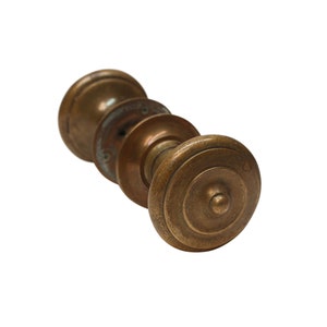 May include: A vintage brass door knob with a round, ornate design. The knob is worn and has a patina finish.