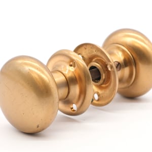 Pode incluir: Um par de maçanetas de porta de latão antigo com forma redonda e acabamento liso.