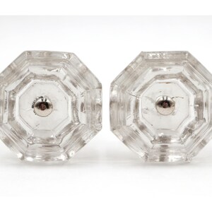 May include: Two clear, octagonal glass cabinet knobs with a silver-colored metal screw. The knobs are transparent, allowing light to pass through. The design is simple and classic, suitable for various furniture styles.