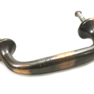 May include: A dark bronze cabinet pull with a copper finish. The pull has a simple, curved design and is attached to a surface with two screws.