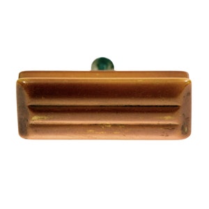 May include: A brown rectangular stamp with a green knob. The stamp has a ridged design on the front and is set against a white background. The stamp appears to be made of wood or a similar material.