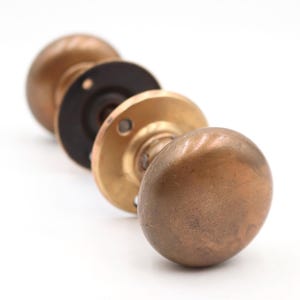 May include: A close-up of four antique bronze door knobs. The knobs are arranged in a row, with varying shades of bronze and copper. The hardware includes round knobs and circular backplates, showcasing vintage design.