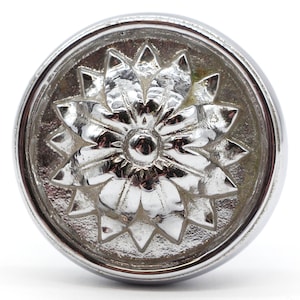 Peut inclure: Un bouton rond argenté avec un motif floral en relief détaillé. Le bouton a une finition lisse et polie.