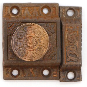 May include: Antique cast iron door latch with a decorative, ornate design. The latch has a round, brass-colored knob with a floral pattern.
