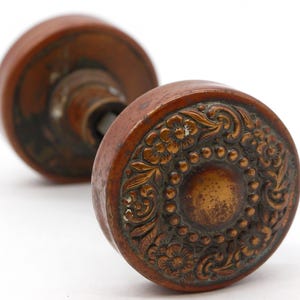 May include: A vintage brass door knob with an ornate floral design. The knob is a dark brown colour and has a circular shape.