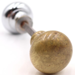 Könnte beinhalten: Ein antiker Türknauf mit Messingausführung an einem Ende und Chromausführung am anderen. Der Knauf ist durch eine Metallstange verbunden. Das Messingende hat ein gesprenkeltes Aussehen.