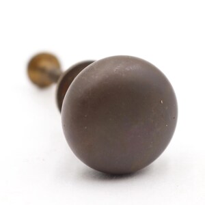 May include: Close-up of a vintage bronze door knob with a round, dark brown handle. The knob is in focus against a white background, showcasing its aged appearance. The hardware suggests a classic or antique style.