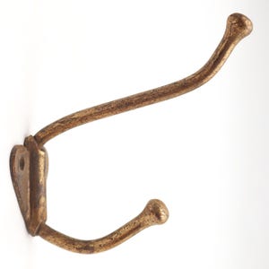 May include: A vintage-style, double-hook wall hanger with a distressed, golden-bronze finish. The hook has a curved design with rounded ends and a decorative mounting plate. Ideal for coats, hats, or other items.
