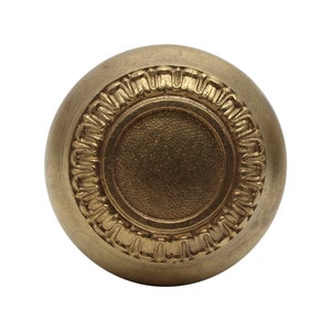 Peut inclure: Un bouton rond en métal doré avec un motif décoratif en relief autour du bord. Le bouton a un centre circulaire lisse.