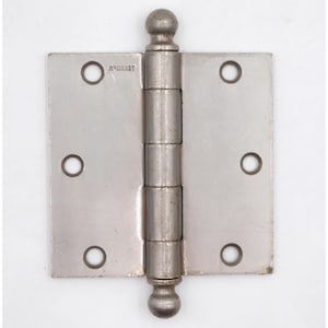 Peut inclure: Une charnière de porte argentée avec un fleuron en forme de boule en haut et en bas. La charnière a un barillet central avec cinq sections et deux plaques rectangulaires, chacune avec trois trous de vis. Le mot "McKinney" est estampillé sur la charnière.