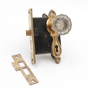 Könnte beinhalten: Ein antiker Türknauf aus Messing mit einem durchsichtigen Kristallknauf aus Glas und einem Schlüsselloch. Der Knauf ist an einer Messingplatte mit einer Schließplatte befestigt.