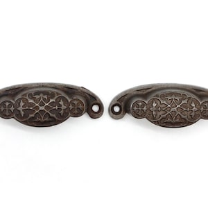 May include: Two antique cast iron drawer pulls with a decorative floral design. The pulls are a dark grey colour and have a slightly distressed finish.