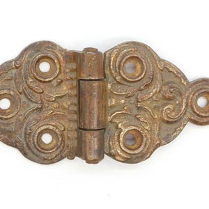 May include: Antique brass hinge with ornate scrollwork and four decorative holes. The hinge is in a worn, aged condition.