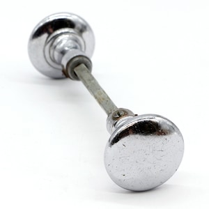 May include: A pair of silver door knobs with a connecting metal rod. The knobs are round and have a slightly textured surface.