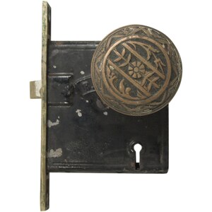 Peut inclure: Une poignée de porte en laiton vintage avec un motif floral décoratif. La poignée est fixée à une plaque de porte en métal noir avec un trou de serrure.