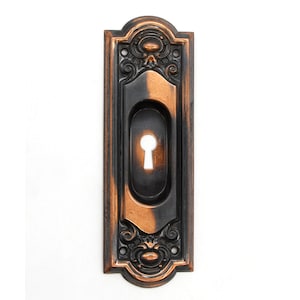 Könnte beinhalten: Ein antiker Schlüsselschlitzabdeckung mit einem verzierten Design. Die Abdeckung ist aus Metall und hat eine dunkelbraune Oberfläche mit kupferfarbenen Akzenten.