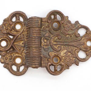 May include: Ornate brass hinge with intricate floral designs and a decorative, ribbed hinge. The hinge is in a worn, antique finish.