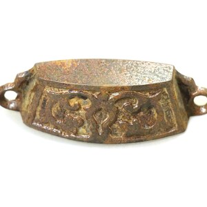 May include: A rusty cast iron drawer pull with an ornate design. The pull is shaped like a small, oval-shaped bowl with a decorative border.