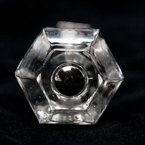 Peut inclure: Une poignée de porte en verre transparent de forme hexagonale avec un centre rond de couleur argent.