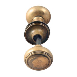 Peut inclure: Une poignée de porte en laiton avec un design rond et décoratif. La poignée est fixée à une broche en métal.
