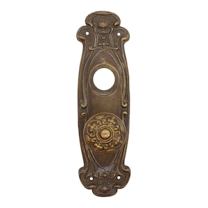 May include: Antique brass door knob and backplate with an ornate design. The knob has a circular centre with a raised design.