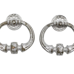 May include: Two silver-toned, ornate, ring-shaped door pulls with a decorative, round, floral design on the top. The pulls have a worn, distressed finish.