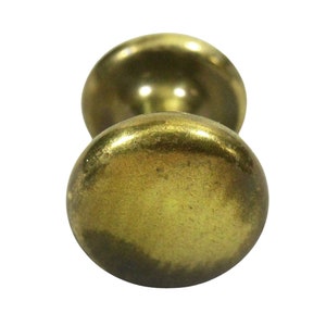 May include: A brass knob with a round, slightly domed shape. The knob has a smooth, polished finish and a slightly aged patina.