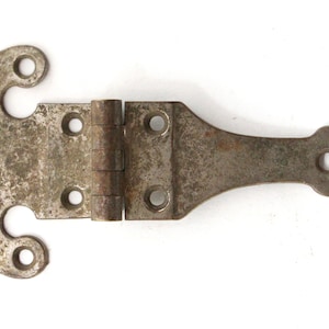 May include: A rusty metal hinge with a decorative, ornate design. The hinge has two loops on one side and a pointed end on the other.