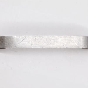May include: A silver metal bar with a slightly curved shape and a brushed finish.