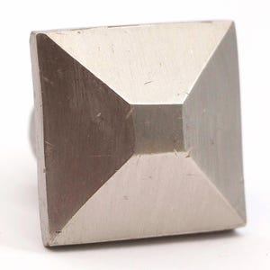 Op de afbeelding: Een zilveren vierkante knop in de vorm van een piramide met een glad, licht getextureerd oppervlak.
