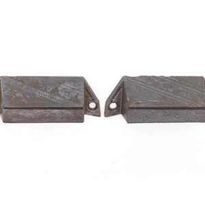May include: Two antique cast iron drawer pulls with an ornate design. The pulls are a dark gray color with a slightly rusted finish.