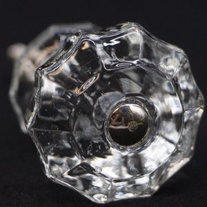 May include: Close-up of a clear, faceted glass doorknob with a silver metal base. The knob has a starburst design and reflects light, creating a sparkling effect. The background is dark, highlighting the clarity of the glass.