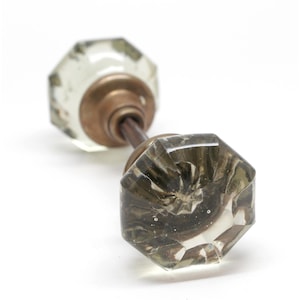 May include: Antique glass door knob with a faceted, octagonal design. The knob has a clear, slightly tinted appearance with a brass-colored base and connecting rod. The glass has a swirl pattern.