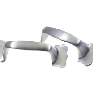 Puede incluir: Dos tiradores de puerta de armario de metal plateado con un borde festoneado decorativo.