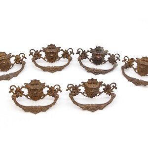 May include: Six antique brass cabinet pulls with ornate designs featuring a face in the center of each pull.